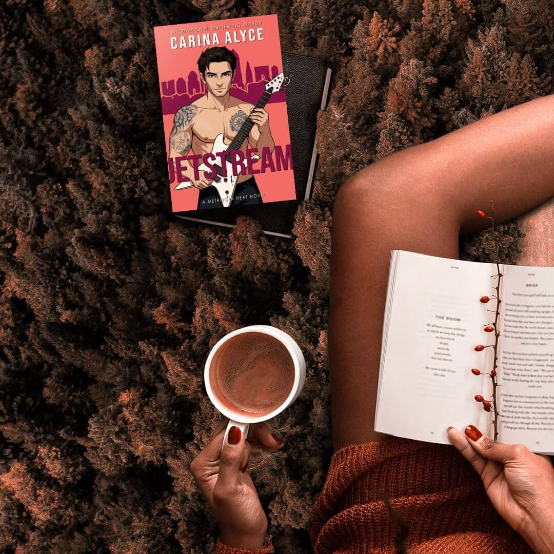Person reading a book with a coffee cup on a textured surface, holding a book titled 'Jetstream' by Carina Alyce.