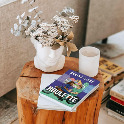 Books and a candle on a wooden table with a vase of flowers in the background