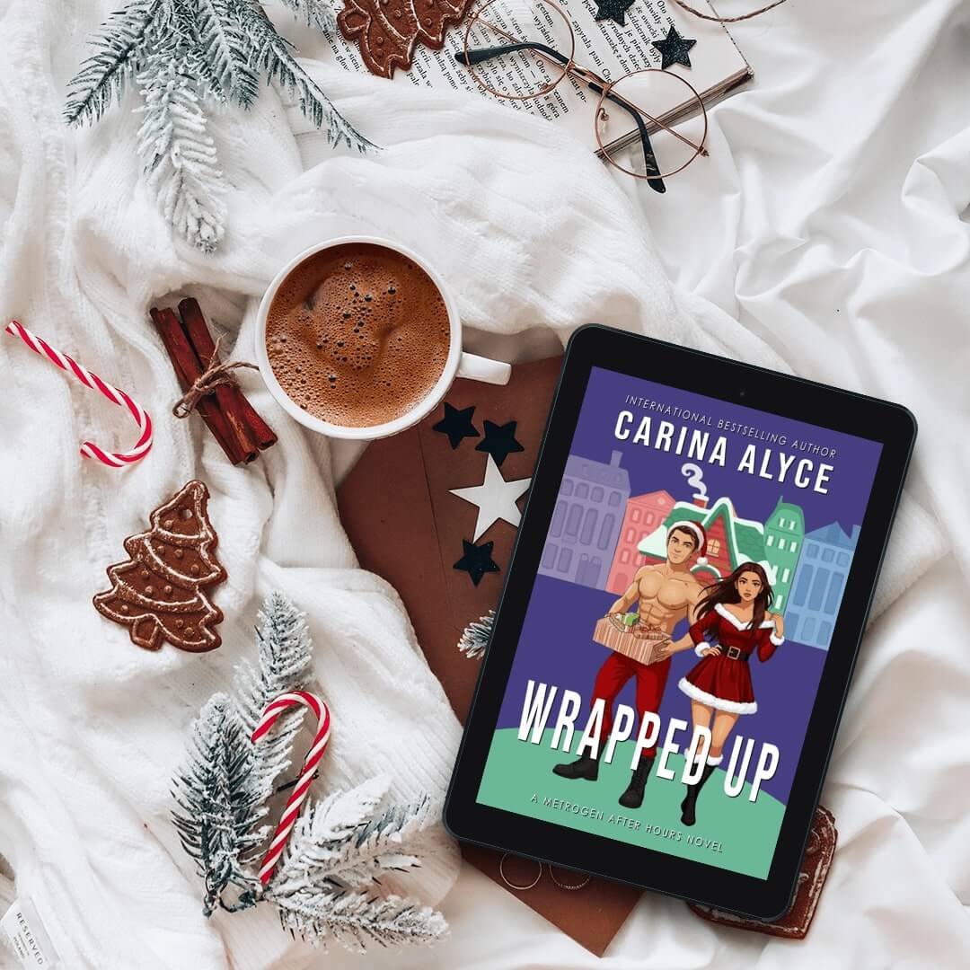 Tablet displaying a book cover titled 'Wrapped Up' by Carina Alyce, with a mug of hot chocolate and Christmas decorations on a white blanket.