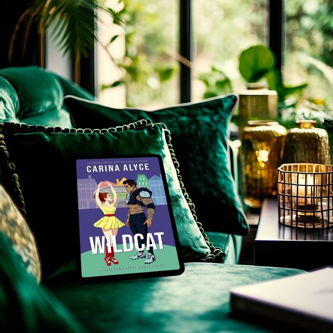 Tablet displaying 'Wildcat' by Carina Alyce on a green couch with decorative pillows and plants.