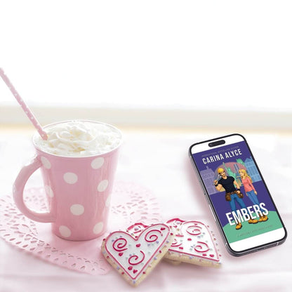 Pink polka dot mug with whipped cream, heart-shaped cookies, and a phone displaying 'Carina Alice Embers' on a white surface.