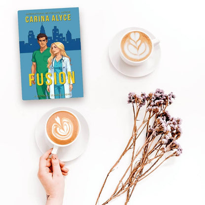 Book titled 'Fusion' by Carina Alyce with two cups of coffee and a bouquet of flowers on a white surface.