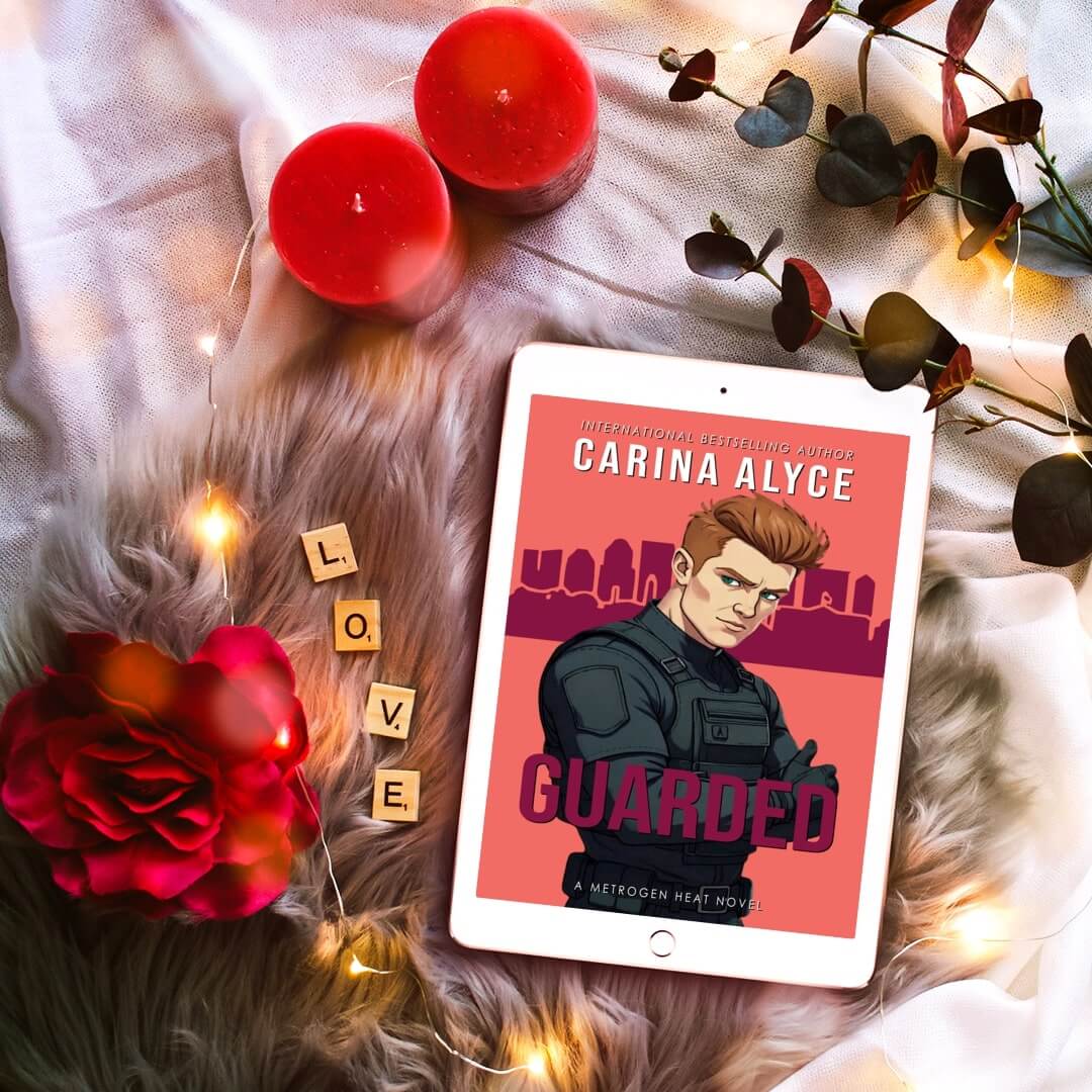 Tablet displaying a book cover titled 'Guarded' by Carina Alyce, surrounded by candles and flowers on a soft surface.