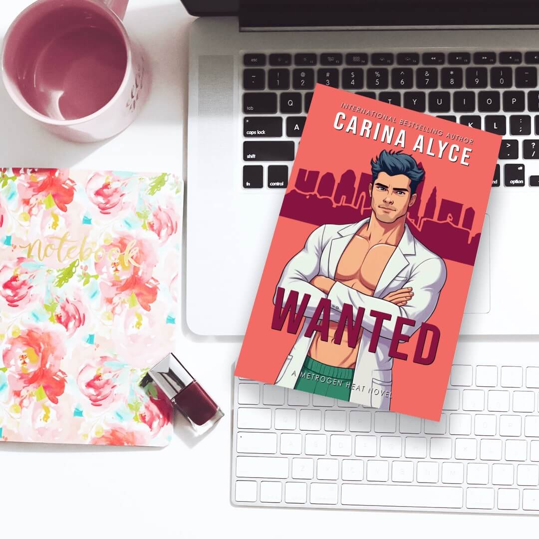 Book titled 'Wanted' by Carina Alyce on a laptop keyboard with a notebook and mug in the background.
